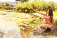 Woman kneeling by pond in Lace-Up Balconette Bra & Thong Set Petal Kiss, emphasizing the bold and romantic lingerie style from Lavinia Lingerie.